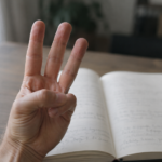 指を3本立てた手元と、開いたノート。文字は判読不能。ミュートカラー
